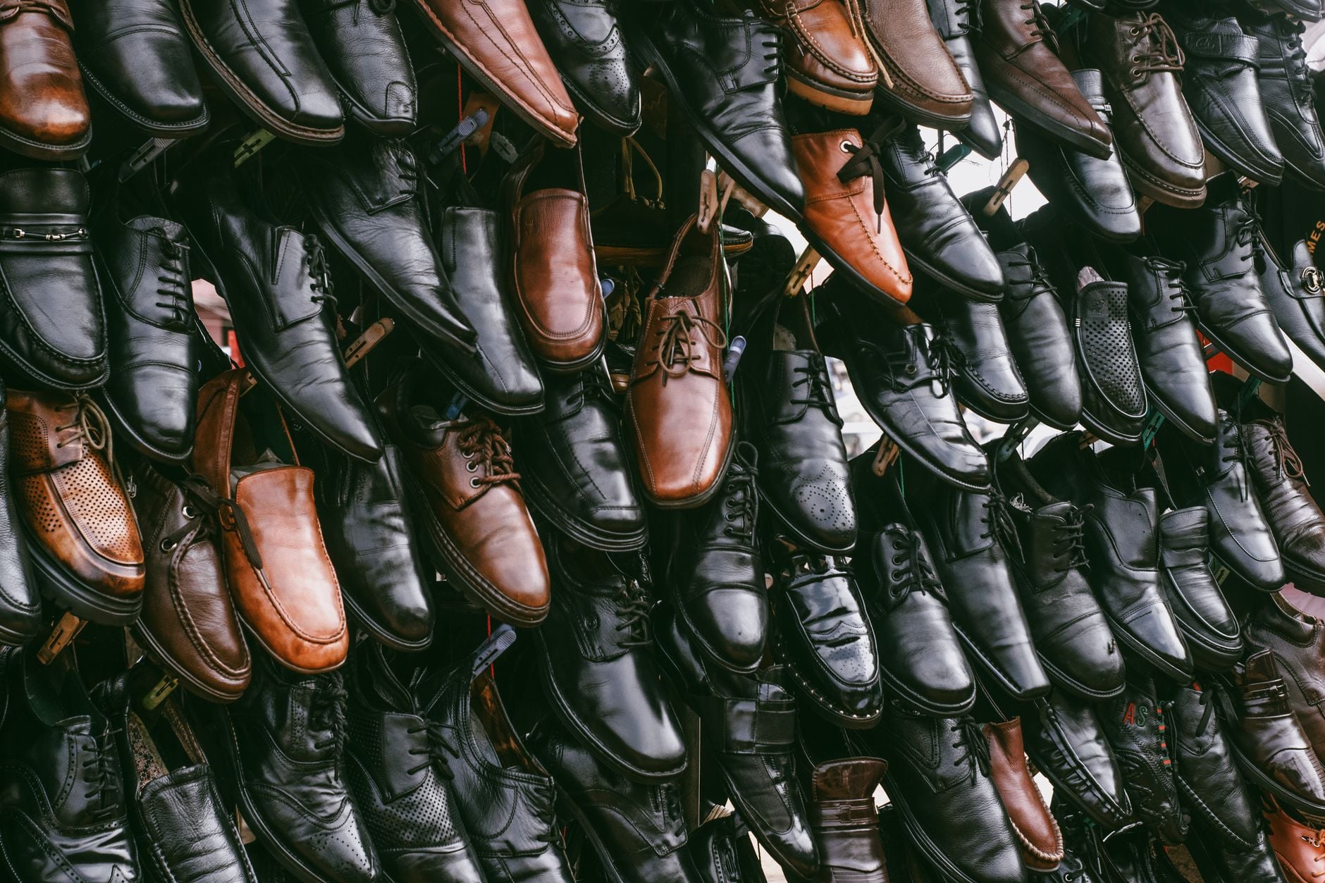 Collezione di scarpe in pelle marrone e nera appese in file ordinate a un mercato