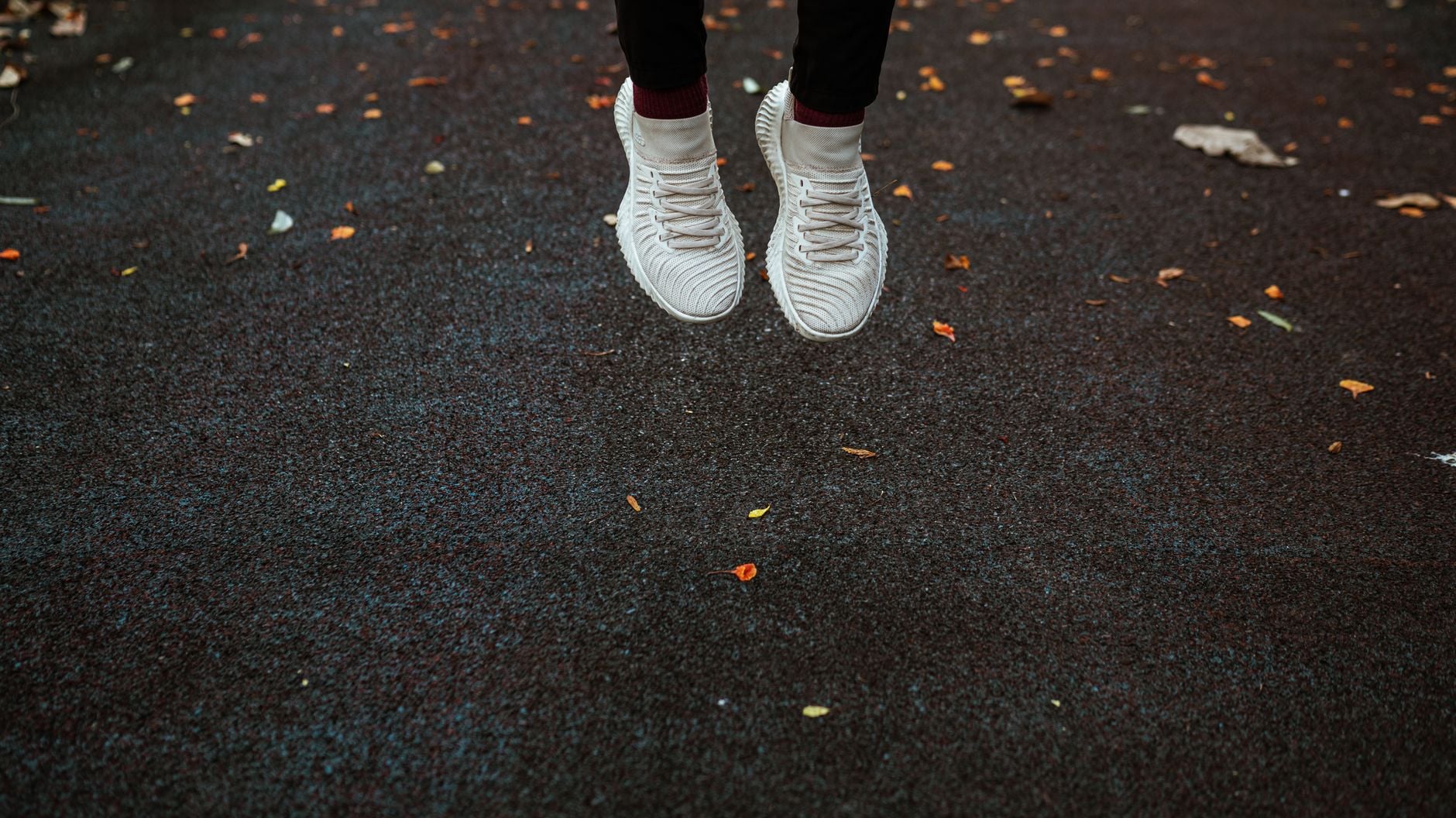 Persona che indossa scarpe bianche con motivi ondulati su strada con foglie autunnali