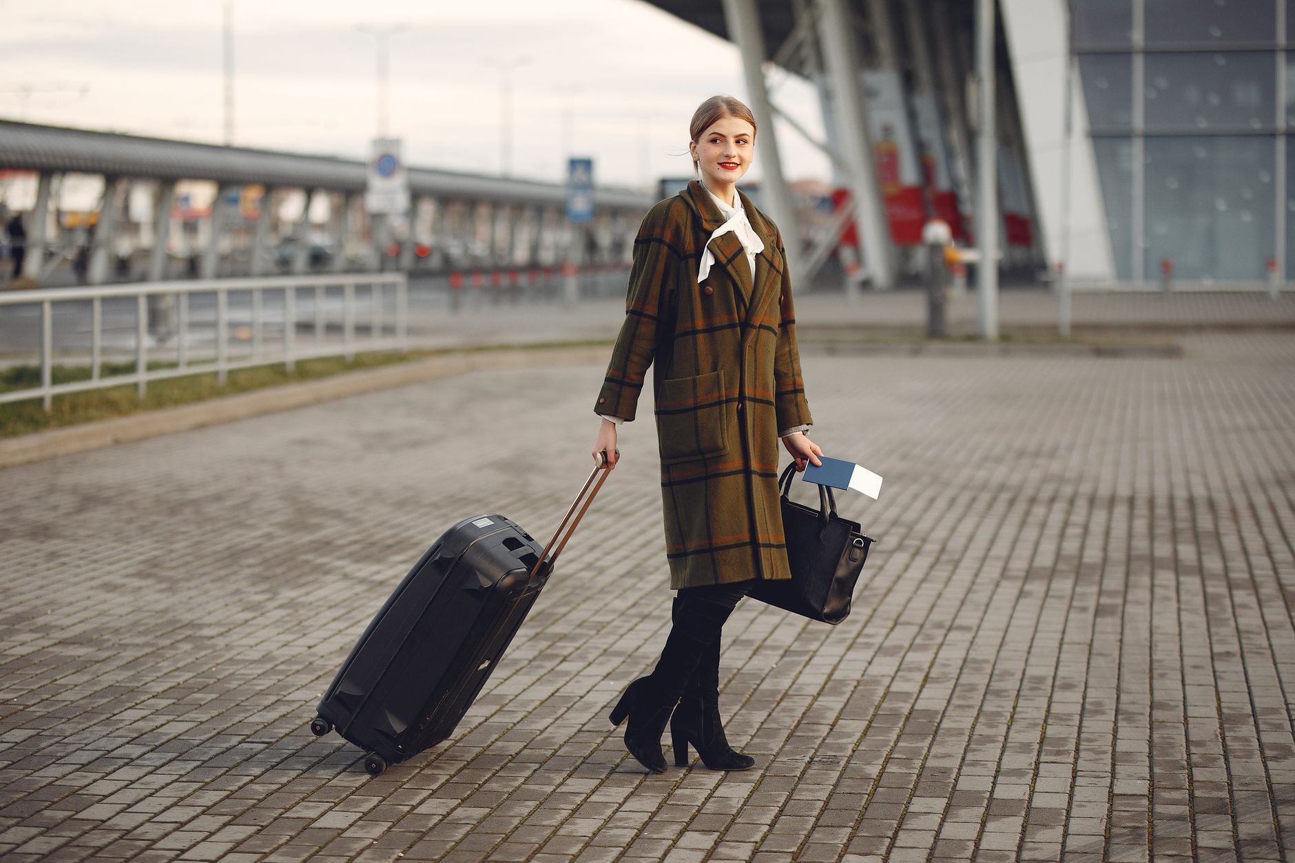 Donna in cappotto a quadri con valigia e borsa in aeroporto