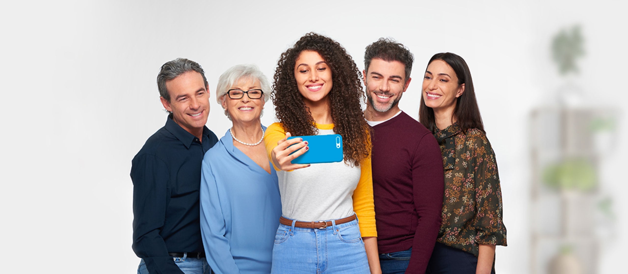 Gruppo di cinque persone di diverse età sorridenti mentre tengono uno smartphone blu