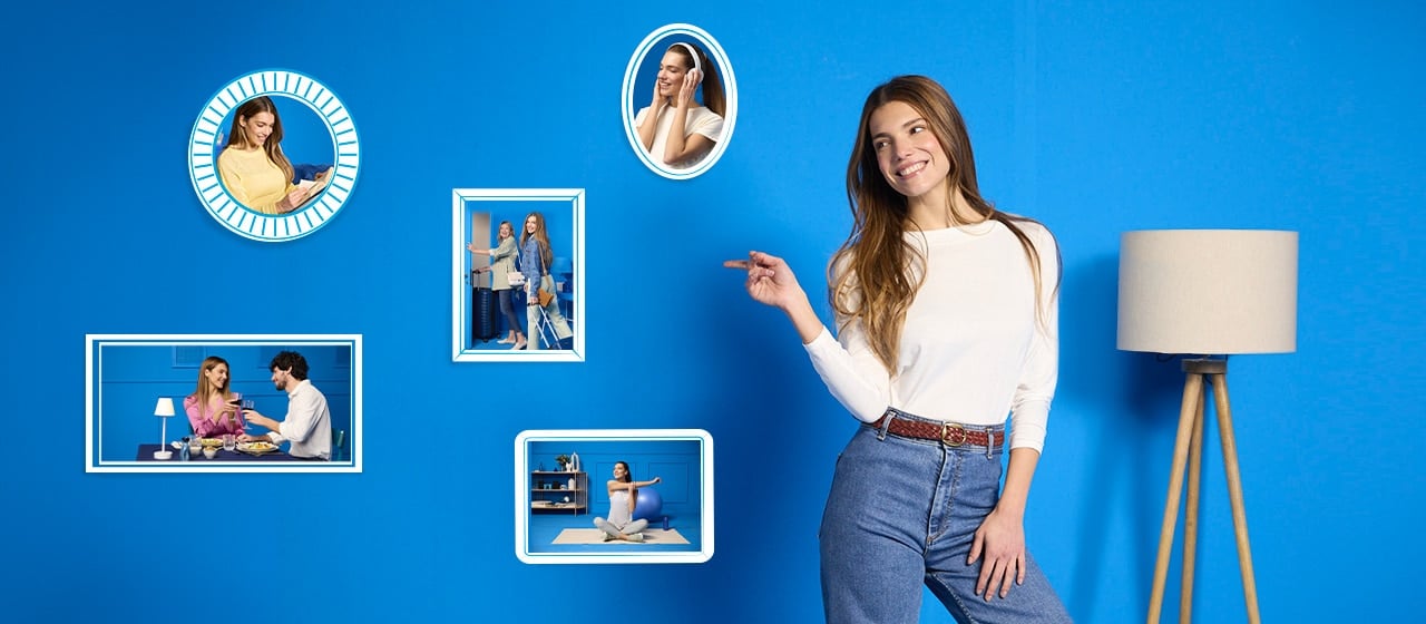 Donna sorridente in maglietta bianca davanti a parete blu con cornici foto e lampada