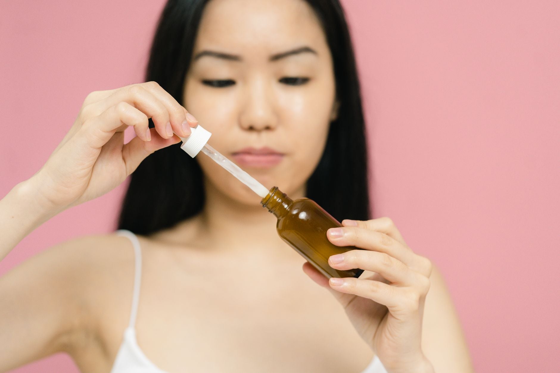 Donna con capelli neri applica siero da una bottiglia scura con contagocce su sfondo rosa