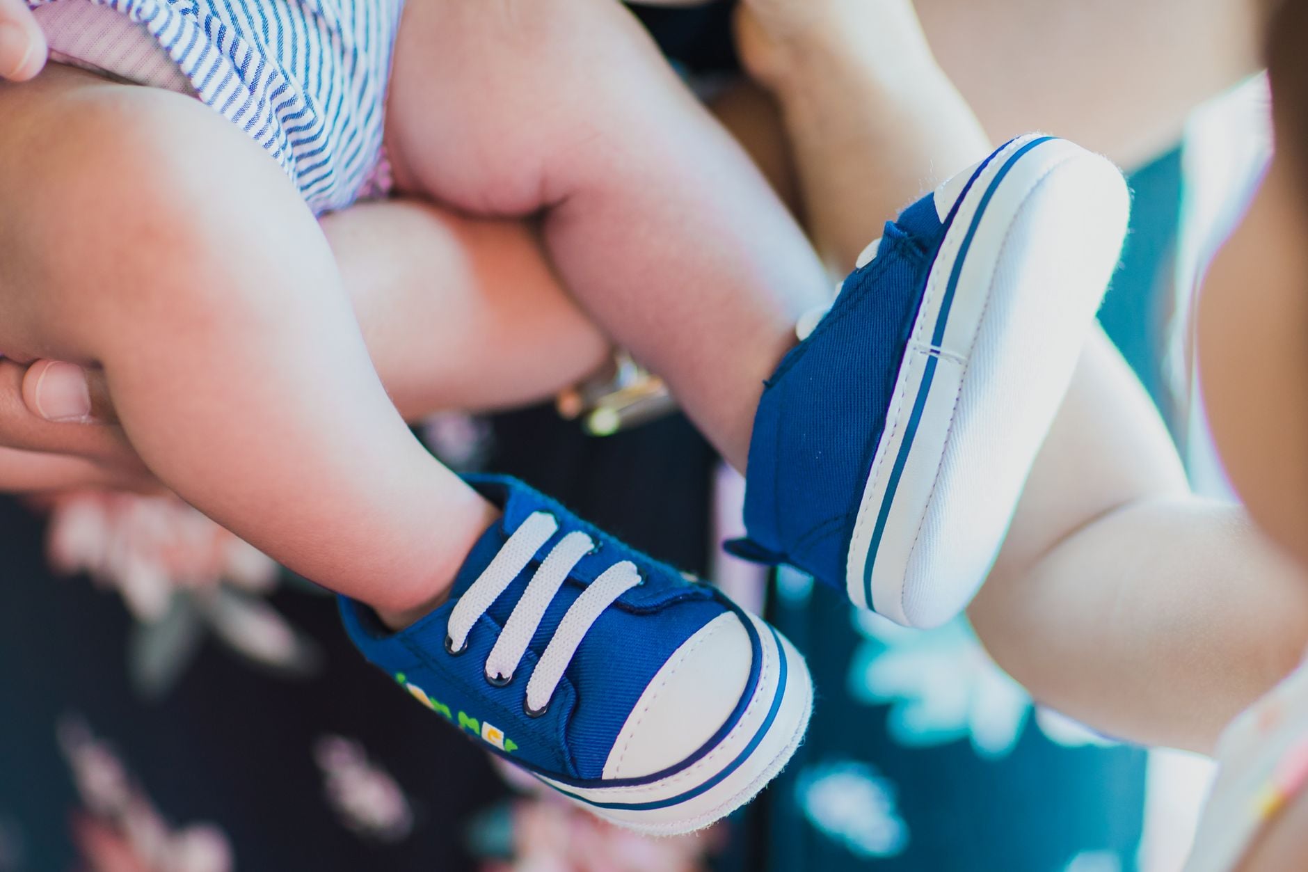 Mani che tengono scarpe blu e bianche da bambino con lacci