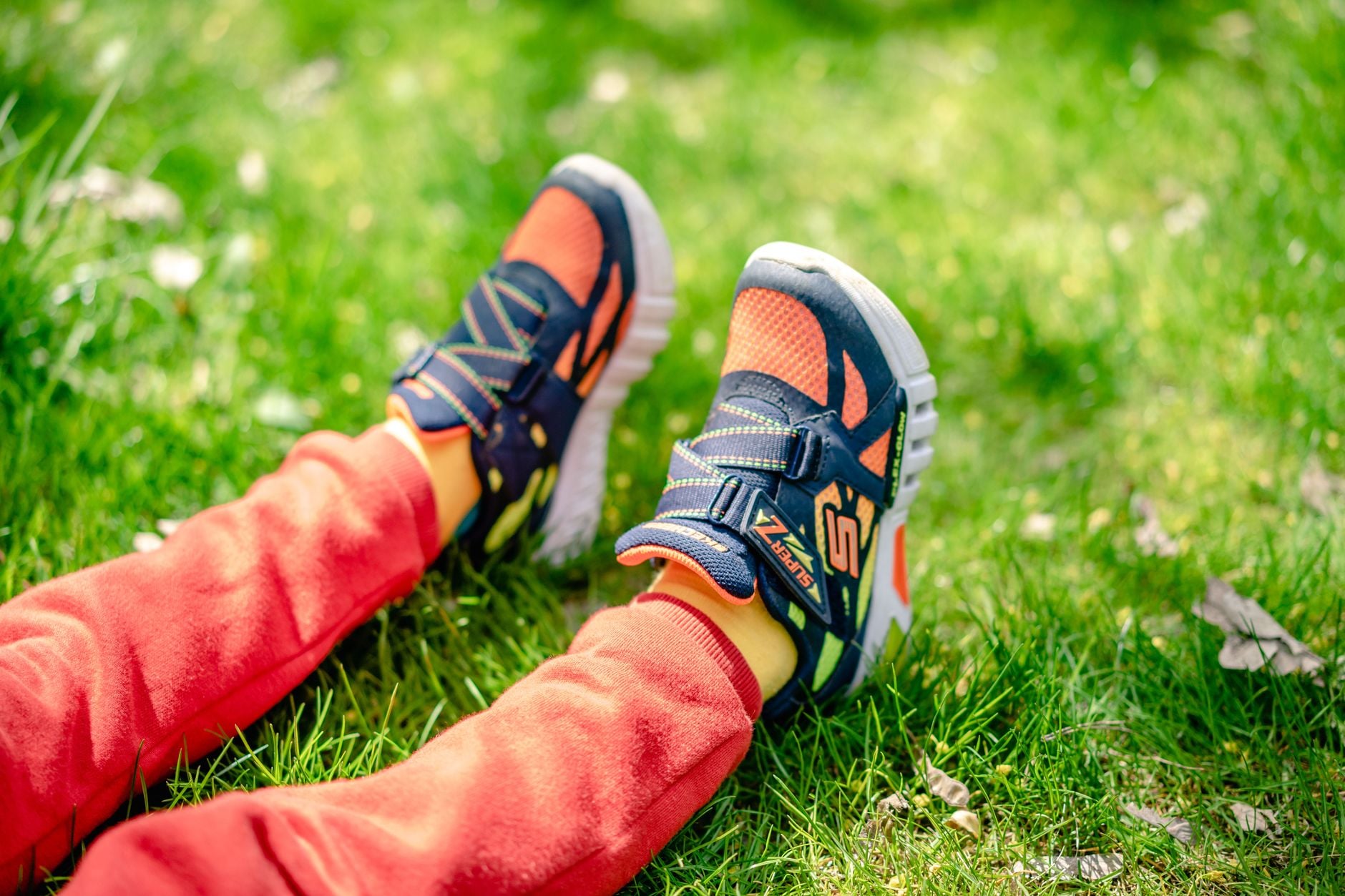 Bambino sdraiato sull'erba che indossa scarpe da corsa blu, arancioni e gialle con calzini colorati
