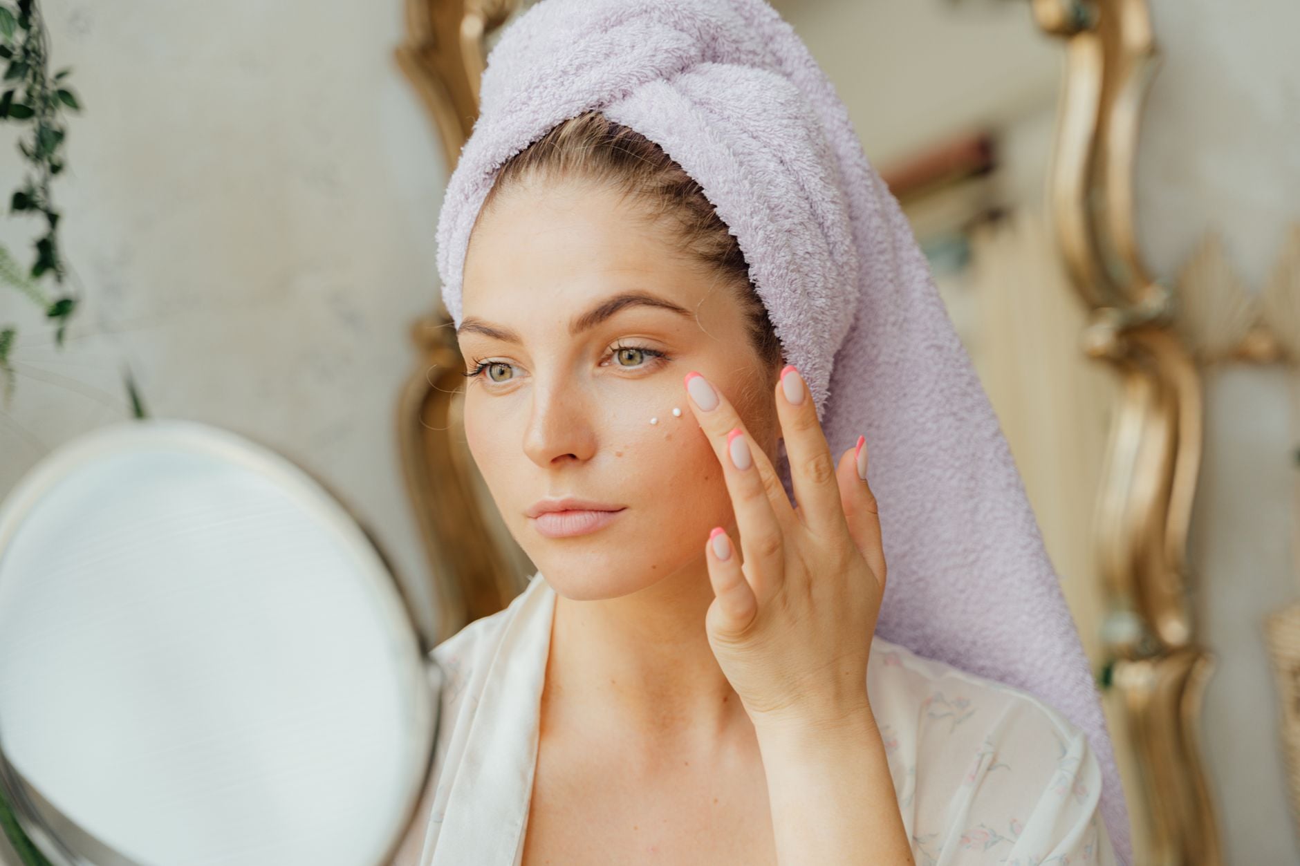 Donna con asciugamano lavanda sui capelli applica crema viso davanti allo specchio