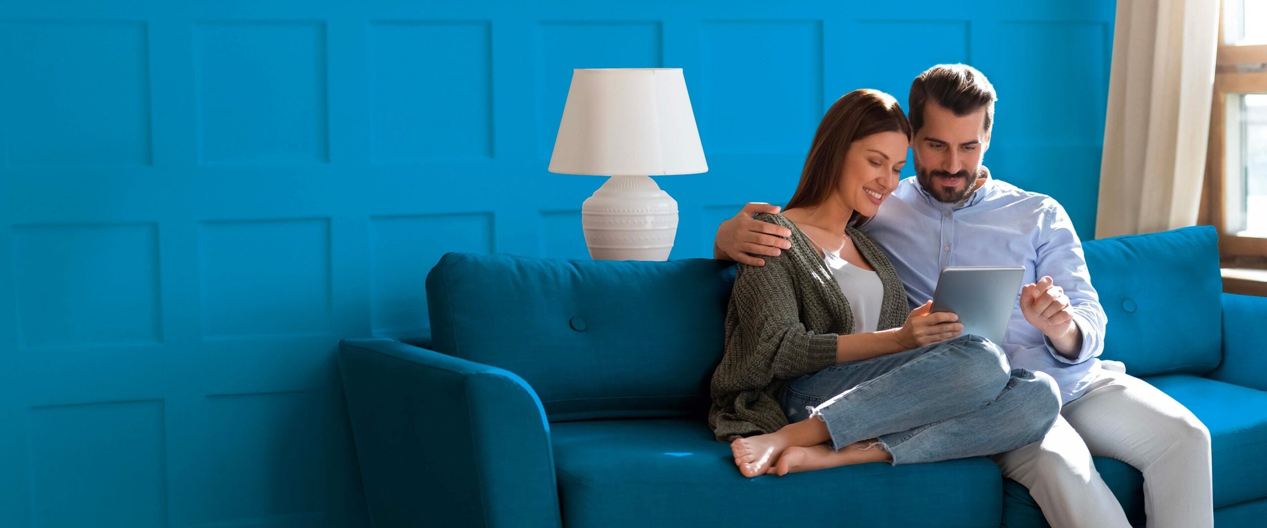 Coppia che sorride seduta su un divano blu mentre guarda un tablet